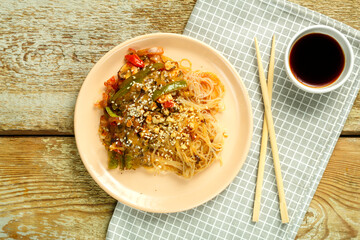 Funchoza with vegetables and mushrooms in a plate on a napkin near sticks and soy sauce.