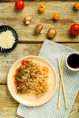 Funchoza with vegetables and mushrooms in a plate on a napkin near sticks and soy sauce vegetables and sesame seeds.