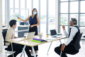 Asian team and Caucasian boss is businesspeople teamwork wearing mask for preventing covid19 virus and brainstorming in meeting room at office. New normal and social distancing for business concept.