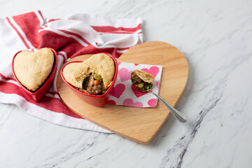 Beef Pot Pies in Red Heart-Shaped Dishes; One with Spoon; On Heart-Shaped Board on White Counter Top; Valentine Napkin