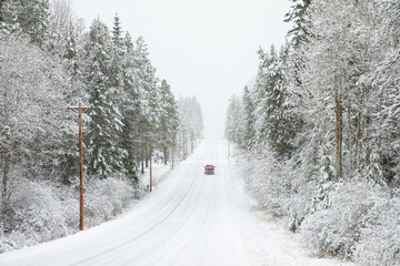 Original winter photograph on a red pick up truck driving down a long snowy road in the forest