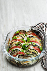 Eggplant and zucchini gratin in glass bowl on white wooden table