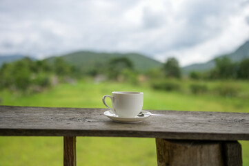 Cup of coffee on a wooden table over mountains landscape and rice field with sunlight. Beauty nature background