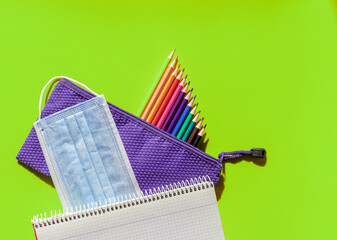 Brightly colored image with children's case, colored pencils, a school notebook and mask against covid 19 - Powered by Adobe