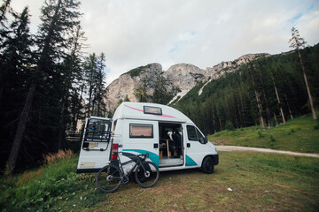 Cute vintage camper van or camping RV parked in wild camping spot in mountain forest. Bicycle off bike rack parked next to converted van. Life on the road in van, outdoor nomadic lifestyle