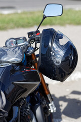 Black moto helmet on motorcycle handlebars against blurred background. Shallow focus.
