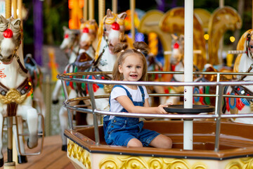 Fototapeta na wymiar happy baby girl riding on carousel at an amusement Park in the summer