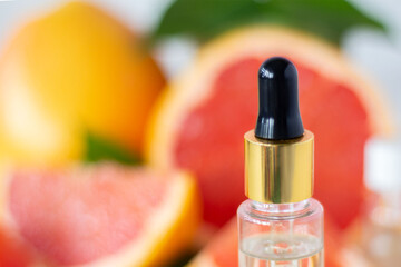 Glass bottle with cosmetic product, citrus essential oil. Drop falling from a pipette. Against the background of fruits. Home skin care concept