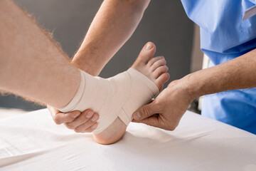 Hands of doctor wrapping foot and ankle of patient with flexible bandage