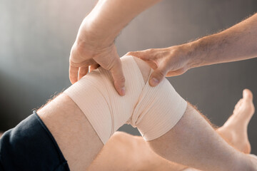 Hands of contemporary clinician massaging knee of young male patient