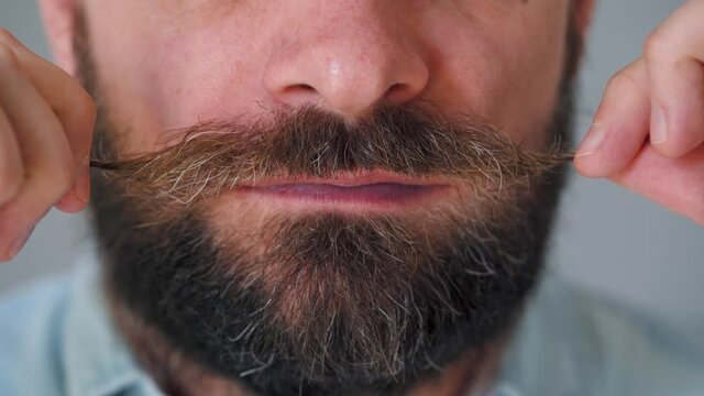 Part of the face of a bearded man who curls his mustache and moves it funny
