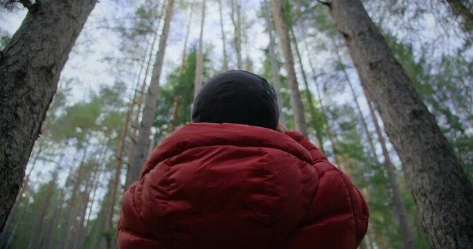 Concept adventure travel blogger wanderlust, man in red puffy jacket create content for social media, record video of forest trees in awe and excitement about nature. Staycation mode and local travel