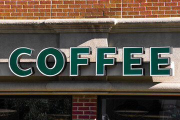 Obraz premium A deep green coffee sign in front of a coffee house with brick walls.