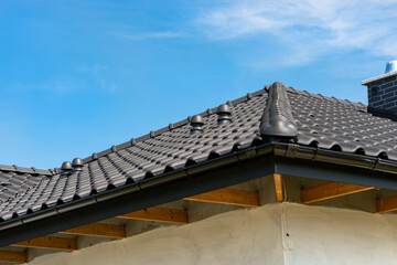 The roof of a single-family house covered with a new ceramic tile in anthracite against the blue sky, visible ceramic ventilation fireplace on the roof.