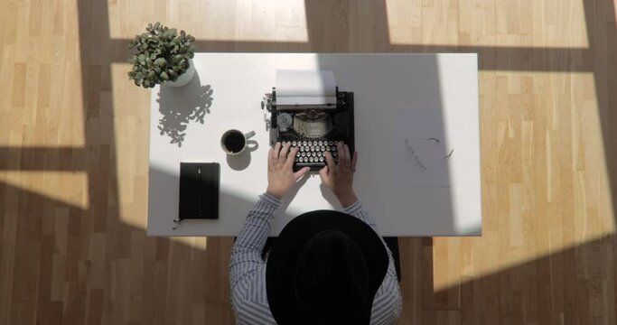 Zoom in top view shot of an author wearing a hat and typing typewriter with floating sun shot in 4k