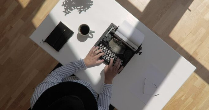 Spinning zoom out top view shot of an author wearing a hat and typing typewriter with floating sun shot in 4k
