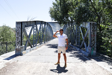 Model man posing in front of bridge with white t shirt and sunglasses.