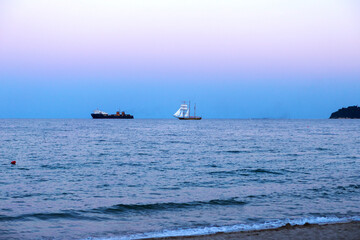 Cargo ship and an anchor boat, with sails sailing floating during a colored sunset off the coast of Varna, Bulgaria. Image shows nice grain pattern at 100 percent