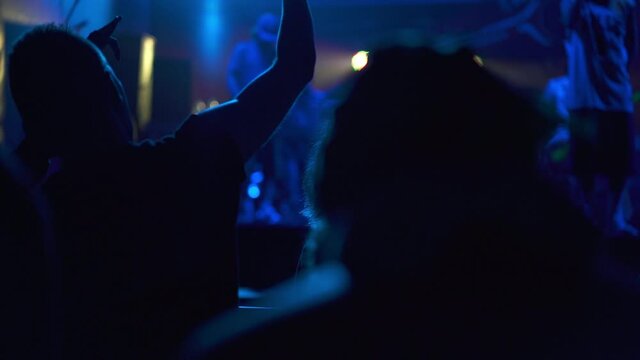 Silhouette of people dancing at a rock band concert. Live performance in a nightclub with fans and stars. People raising their hands and singing songs. Concept of entertainment and background.