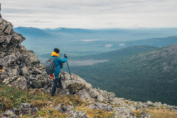 A man in a bright jacket stands with his back on a trail in the mountains