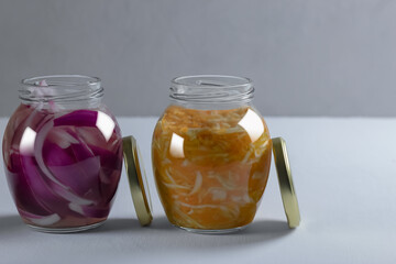 Fermented vegetables cabbage, carrots and purple onions in two jars with open golden lids on a gray and white background. Side view. Horizontal orientation. Copy space.