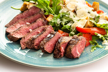 Medium-rare steak and tomato, arugula and parmesan salad on a blue plate