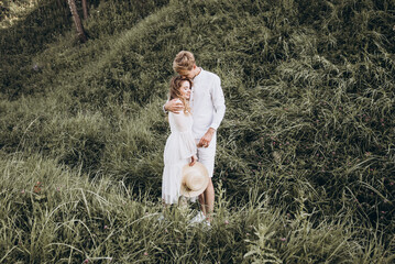 Couple in white are walking on green nature at sunset in summer