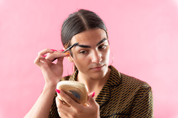 Studio portrait with pink background of a young man putting on makeup.