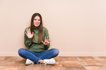 Young caucasian woman sitting on the floor isolated rejecting someone showing a gesture of disgust.