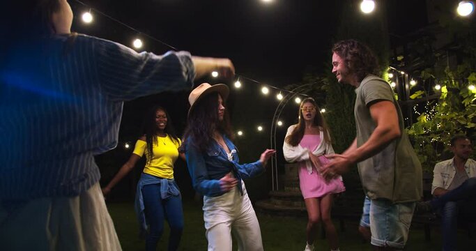 Joyful beautiful mixed-race girls dancing in garden at party. Caucasian girl in hat and boy having fun. African American female dance outdoor. Happy guy moving to music. Celebration concept
