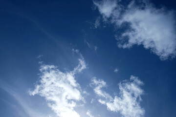 Pure white cumulus clouds in deep blue sky, soft cirrus clouds in background, natural sun glow at...