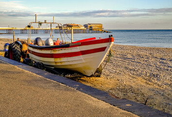 Fototapeta premium Front on view of a traditional crab fishing boat on Cromer beach at sunrise. In the distance is the Victorian era pier, a must see for people visiting this seaside town.