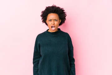 Fototapeta na wymiar Middle aged african american woman against a pink background isolated screaming very angry and aggressive.