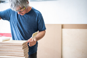 Woodworker applying varnish with a roller to several pieces of wood.Copy space