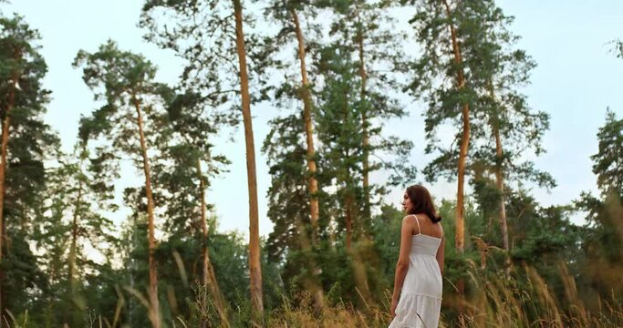 Beautiful romantic girl walks on the grass, a clearing near a pine forest, travel. Walk in a pine forest, the grass glows in the sun. Side view.