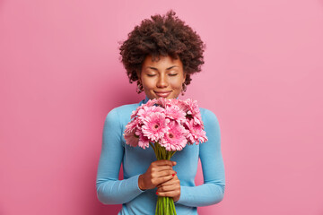 Attractive pleased dark skinned model receives flowers as present, stands with closed eyes, enjoys...