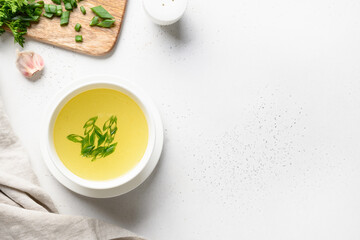 Chicken broth with green onion in white bowl on white table. Copy space. View from above.