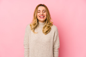 Young blonde cute woman wearing a sweater isolated laughs and closes eyes, feels relaxed and happy.