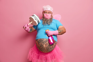 Hard working bearded man busy with housekeeping, dressed in fairy costume to entertain customers,...