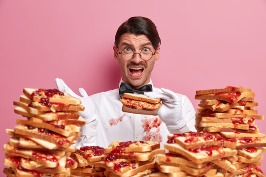 Frustrated Displeased Professional Male Waiter Holds Delicious Sandwich, Exclaims With Negative Emotions, Has Dirty Shirt After Being Not Careful While Eating, Isolated On Pink Background. Cafe Staff