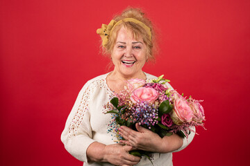 A positive aged woman holds a beautiful bouquet of flowers in her hands, she is happy and fascinated by such a gift, all ages are submissive to love