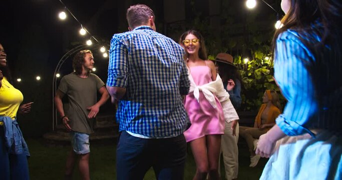 Happy Mixed-races Girls Dancing In Backyard At Party At Night. Caucasian Girl And Boy Making Funny Moves. African American Female Dances. Joyful Guy Moving To Music. Happiness Concept