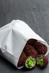Crisp broccoli bite coated in a beetroot crumb in paper bag on black stone background