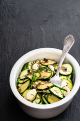 Marinated zucchini slices in clay bowl on black stone background