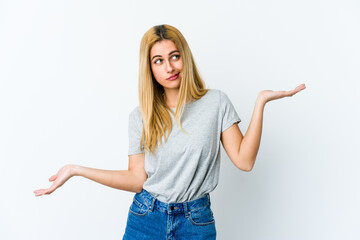 Young blonde woman isolated on white background confused and doubtful shrugging shoulders to hold a copy space.