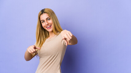 Young blonde woman isolated on purple background pointing to front with fingers.