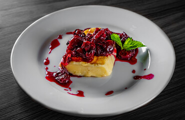 Halloumi cheese frying with cherry in plate on black wooden table