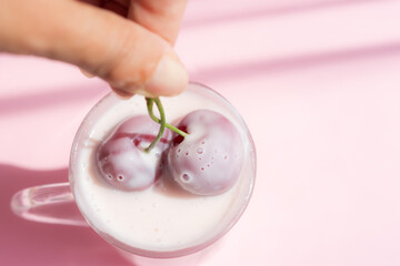 Cherry yogurt in a mug on a pink background. Delicious milk drink with cherry slices. Hot pink isolated background. Proper healthy nutrition. Summer drink. Two cherries as a symbol of love and unity.