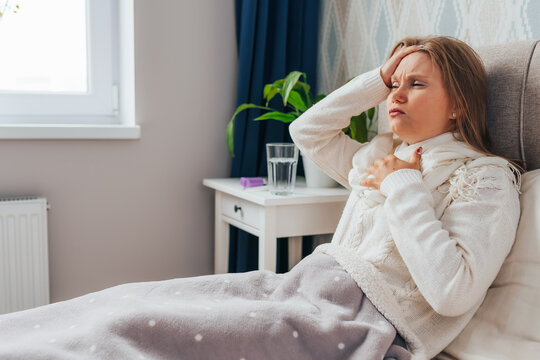 Beautiful blonde young woman have strong headache and chest pain. Female sits in bed and hold head with her hands, suffering on her face