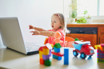 Naklejka premium Happy toddler girl with laptop and toys